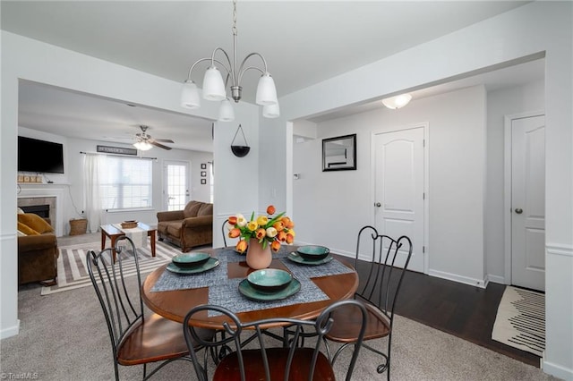 dining room featuring ceiling fan with notable chandelier, wood-type flooring, and a fireplace