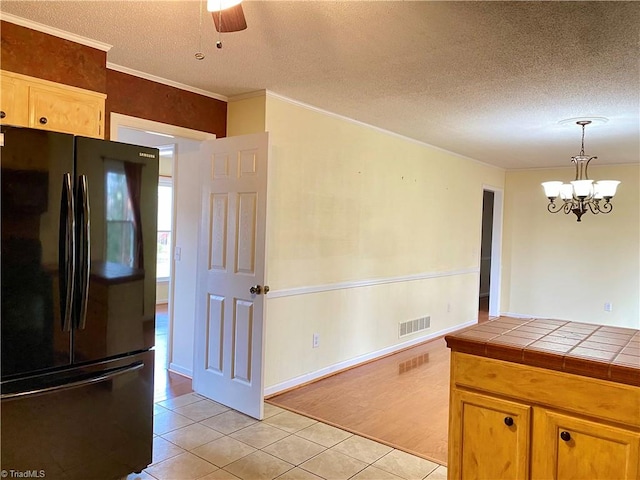 kitchen with tile countertops, black refrigerator, light tile patterned floors, and hanging light fixtures