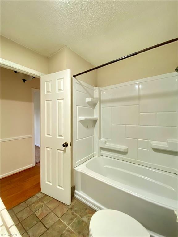 bathroom featuring wood-type flooring, a textured ceiling, bathing tub / shower combination, and toilet