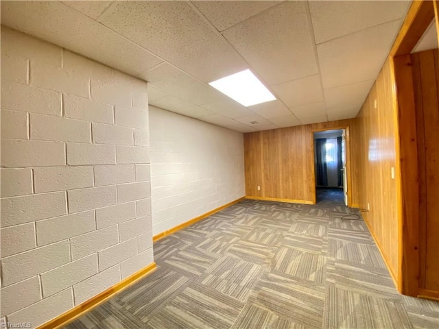 spare room with a paneled ceiling, wooden walls, and dark carpet