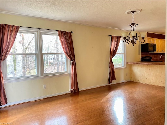 interior space featuring a notable chandelier, light hardwood / wood-style floors, a textured ceiling, and a wealth of natural light