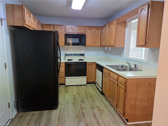 kitchen featuring a textured ceiling, a sink, light countertops, light wood-type flooring, and black appliances