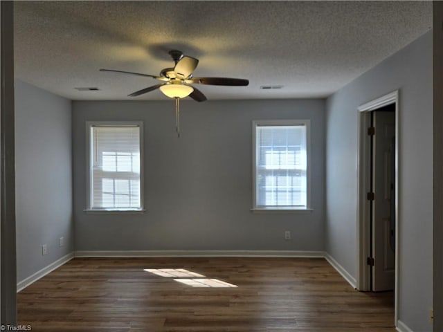 spare room with baseboards, plenty of natural light, visible vents, and dark wood-type flooring