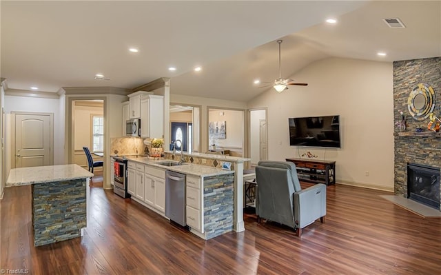 kitchen featuring white cabinets, appliances with stainless steel finishes, light stone counters, a sink, and open floor plan