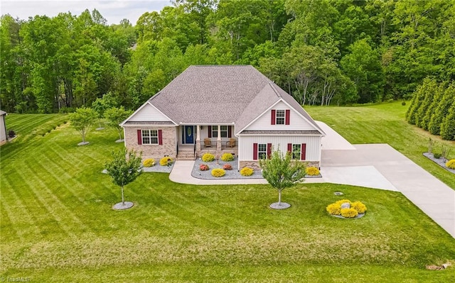 view of front facade with a front lawn, covered porch, board and batten siding, driveway, and a wooded view
