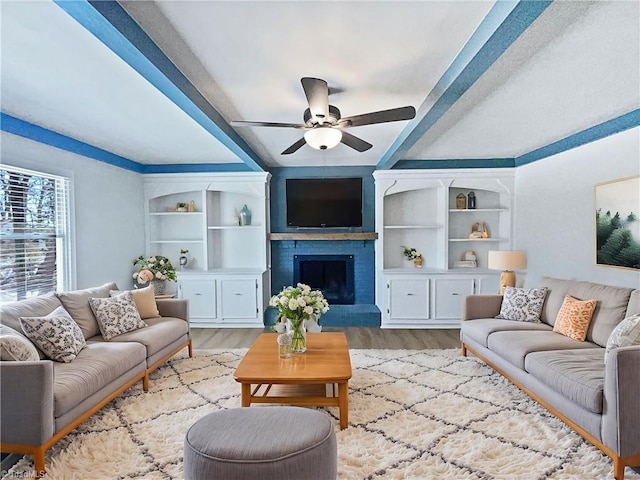 living room with light wood-style floors, ceiling fan, a fireplace, and built in features