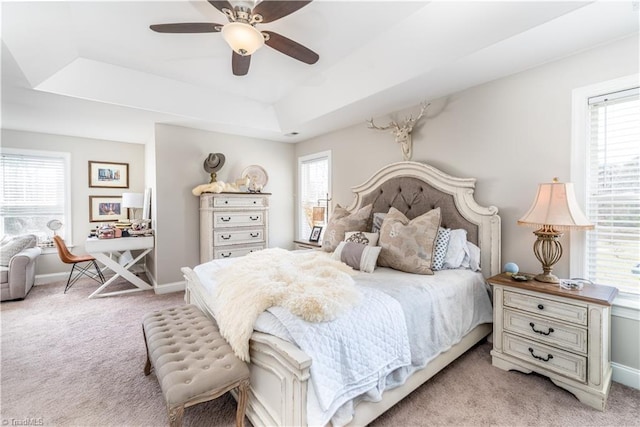 bedroom with a raised ceiling, multiple windows, and light colored carpet