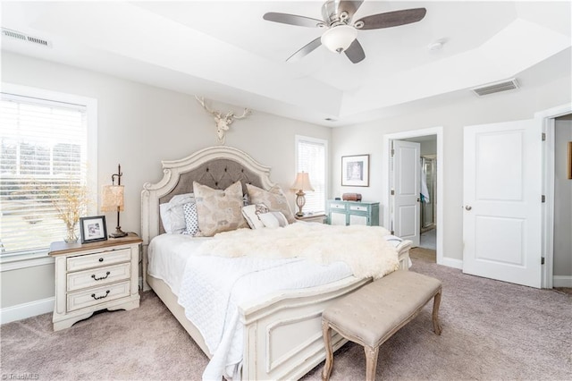 bedroom with light carpet, multiple windows, and a tray ceiling