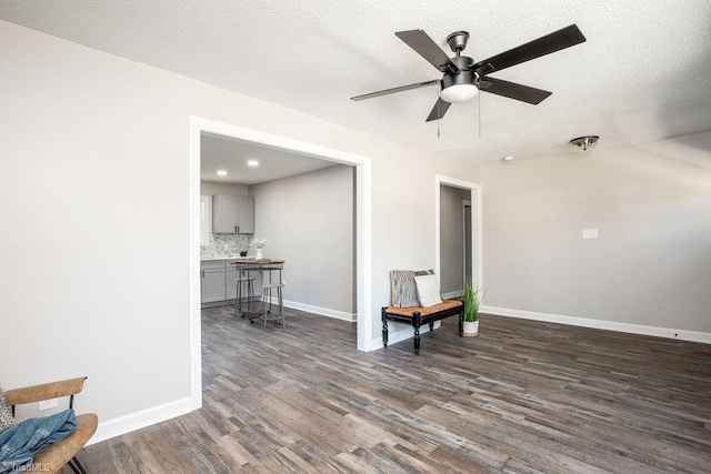 living area with dark wood-type flooring, ceiling fan, and a textured ceiling