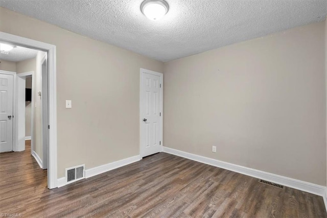 empty room featuring baseboards, wood finished floors, visible vents, and a textured ceiling