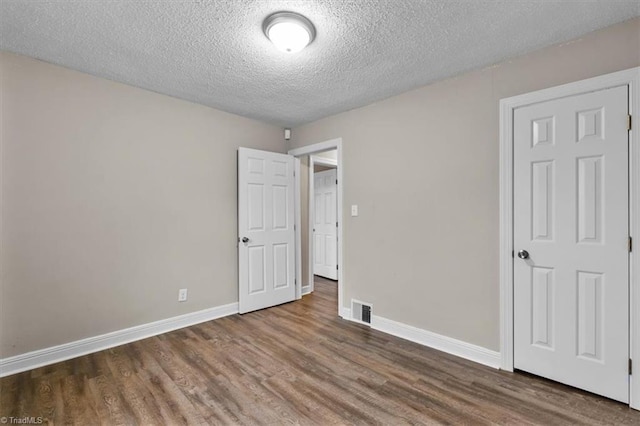 unfurnished bedroom with baseboards, wood finished floors, visible vents, and a textured ceiling
