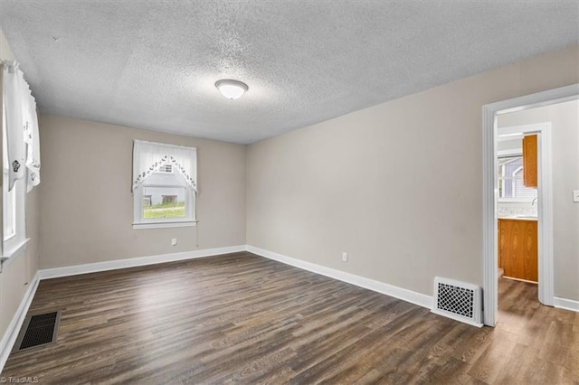 spare room featuring dark wood-type flooring, plenty of natural light, and visible vents