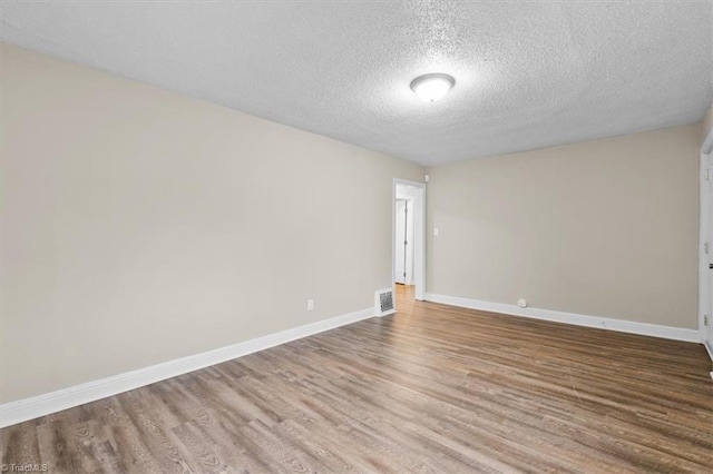 empty room with visible vents, baseboards, wood finished floors, and a textured ceiling
