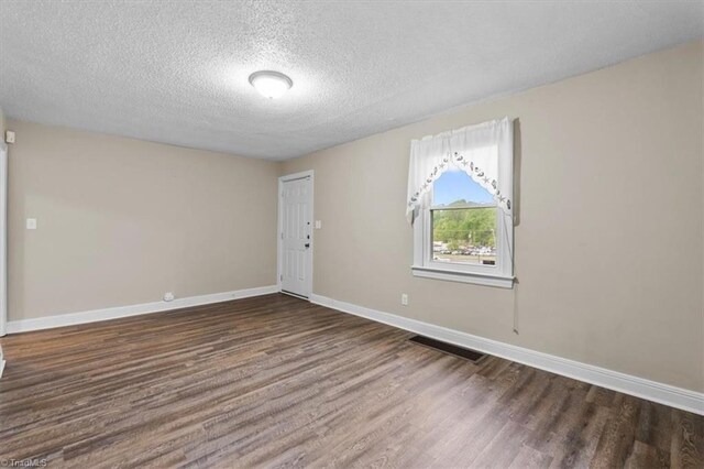 spare room with baseboards, visible vents, a textured ceiling, and dark wood-type flooring
