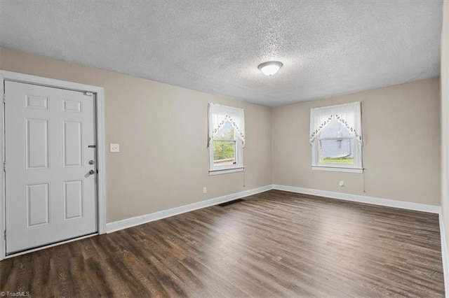 spare room featuring wood finished floors, a textured ceiling, baseboards, and visible vents
