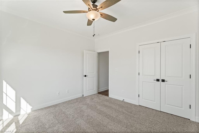 unfurnished bedroom featuring baseboards, a ceiling fan, carpet, crown molding, and a closet