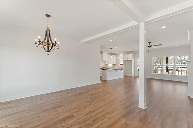 unfurnished living room featuring ceiling fan with notable chandelier, beamed ceiling, and wood finished floors