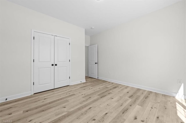 unfurnished bedroom featuring baseboards, light wood-type flooring, and a closet