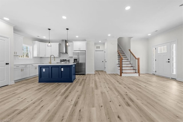 kitchen with light countertops, appliances with stainless steel finishes, white cabinetry, wall chimney range hood, and light wood-type flooring