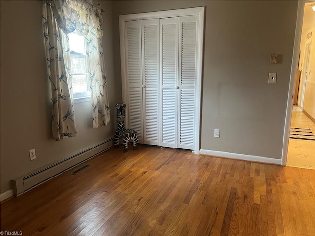 unfurnished bedroom with baseboard heating, a closet, and light hardwood / wood-style flooring