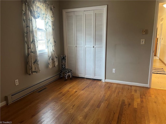 unfurnished bedroom with a baseboard heating unit, a closet, and light wood-type flooring