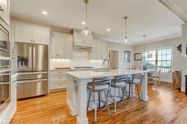 kitchen with appliances with stainless steel finishes, a center island with sink, white cabinets, and decorative light fixtures