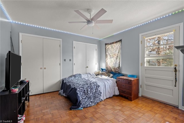 bedroom with a textured ceiling, light parquet floors, and two closets