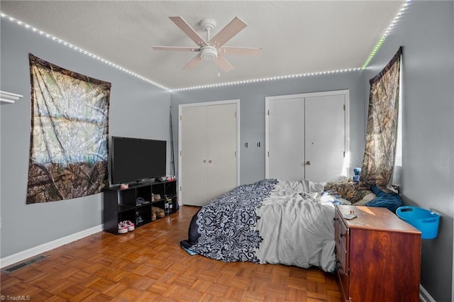 bedroom with ceiling fan, two closets, and light parquet floors