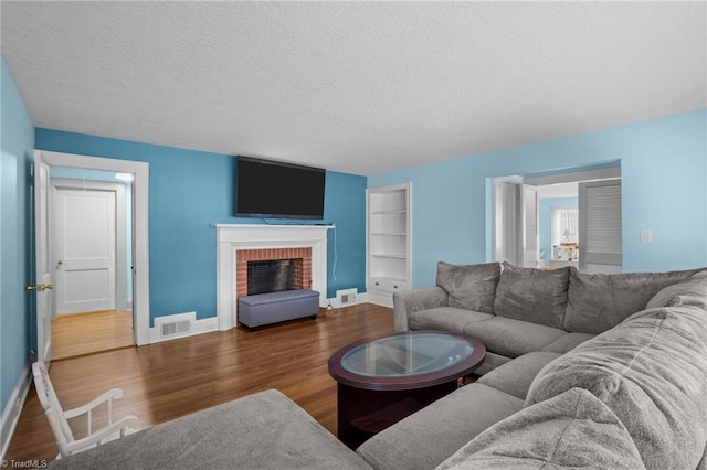 living room with a brick fireplace, built in features, dark hardwood / wood-style floors, and a textured ceiling