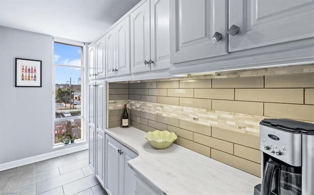 kitchen featuring light tile patterned flooring, white cabinets, light stone counters, and decorative backsplash