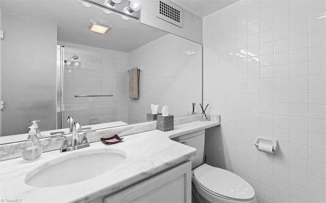 bathroom featuring vanity, toilet, a shower with door, and tile walls