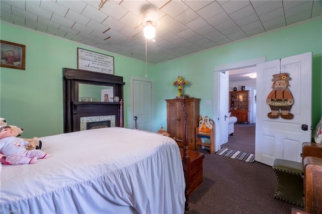 bedroom featuring a stone fireplace and dark carpet