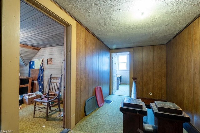 hallway featuring light colored carpet, a textured ceiling, and wood walls