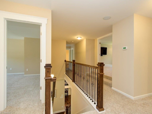 hallway with an upstairs landing, baseboards, and carpet floors