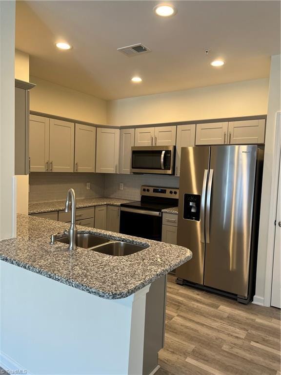2607 Pennoak Way Unit H, Greensboro, NC 27407 - kitchen with stainless steel appliances, a peninsula, dark stone countertops, light wood finished floors, and gray cabinetry