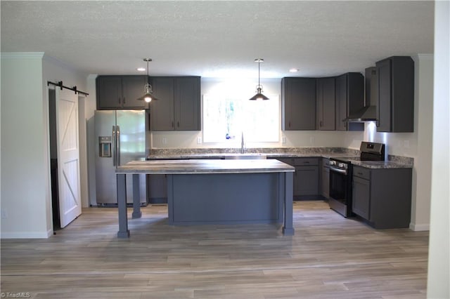 kitchen with sink, stainless steel appliances, a barn door, decorative light fixtures, and a kitchen island