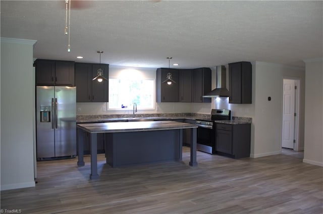 kitchen with wall chimney range hood, light wood-type flooring, decorative light fixtures, a kitchen island, and stainless steel appliances