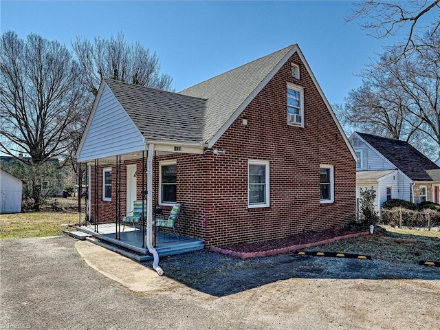 view of front of house featuring a shingled roof, a porch, and brick siding