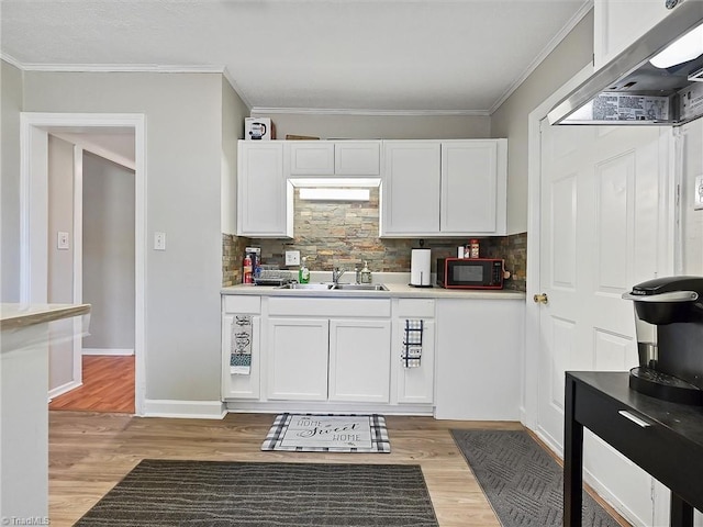 kitchen with light wood-type flooring, white cabinets, crown molding, and light countertops