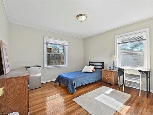 bedroom with baseboards, wood-type flooring, freestanding refrigerator, and crown molding