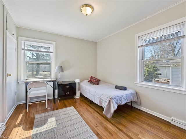 bedroom with wood-type flooring, crown molding, a baseboard heating unit, and baseboards