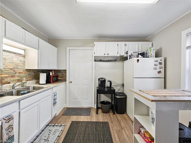 kitchen featuring freestanding refrigerator, white cabinetry, a sink, and under cabinet range hood