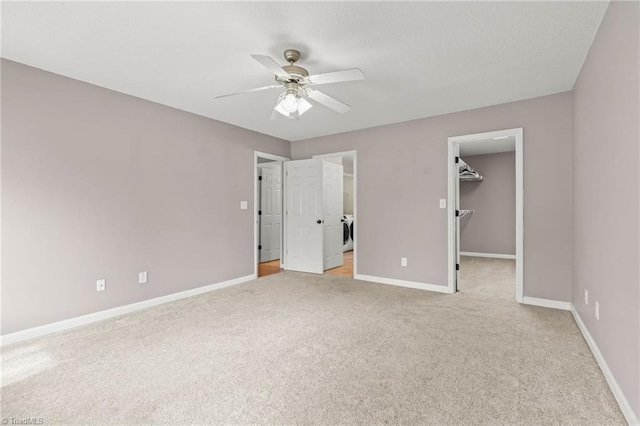 unfurnished bedroom featuring a walk in closet, light colored carpet, ceiling fan, washer and clothes dryer, and a closet