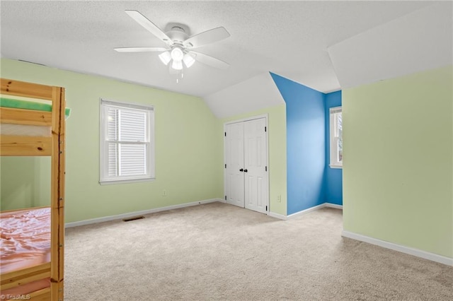 unfurnished bedroom featuring ceiling fan, lofted ceiling, light carpet, and a textured ceiling