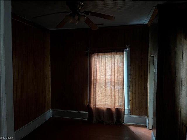 spare room featuring ceiling fan, a healthy amount of sunlight, and wood walls