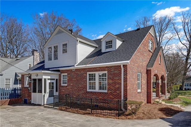 exterior space with fence, brick siding, a shingled roof, and a sunroom