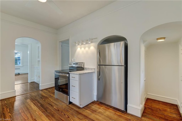 kitchen with light countertops, appliances with stainless steel finishes, wood finished floors, arched walkways, and white cabinetry