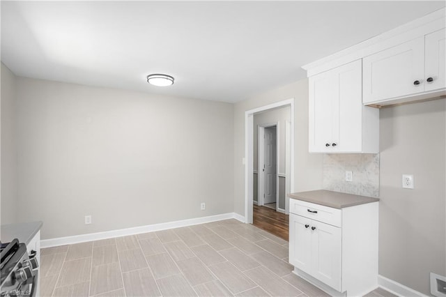 kitchen with stainless steel range, backsplash, white cabinets, and light hardwood / wood-style floors