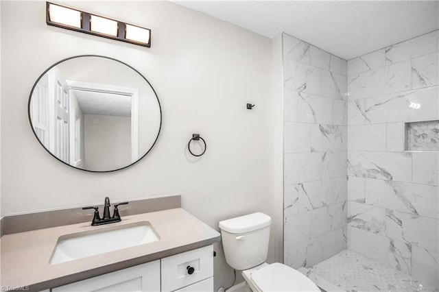 bathroom with vanity, toilet, and a tile shower