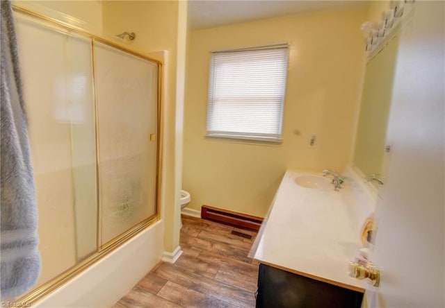 full bathroom featuring toilet, combined bath / shower with glass door, baseboard heating, vanity, and hardwood / wood-style floors